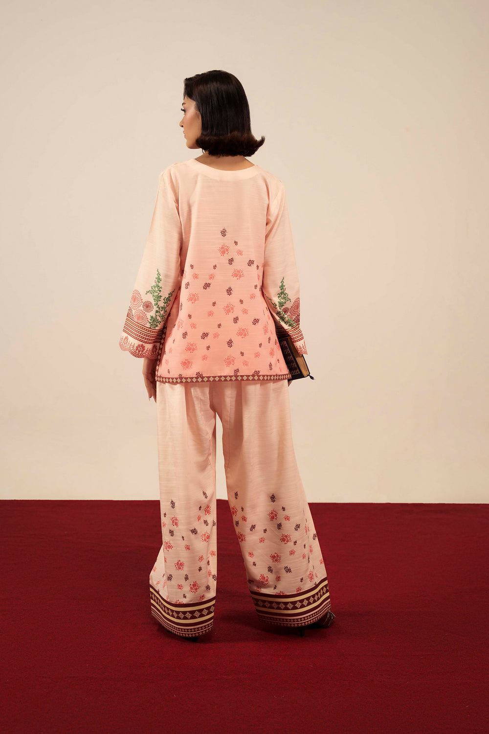 Woman wearing a pink traditional outfit with floral patterns on a red and beige background